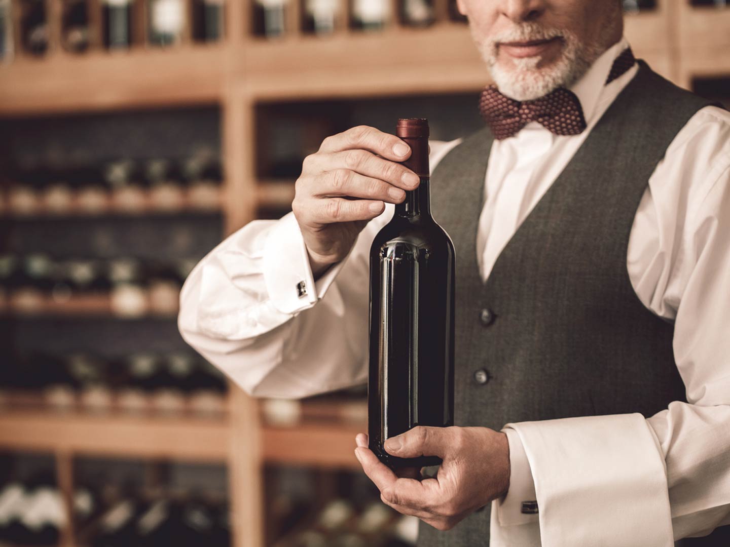 restaurant waiter presenting wine bottle with wine wall in background